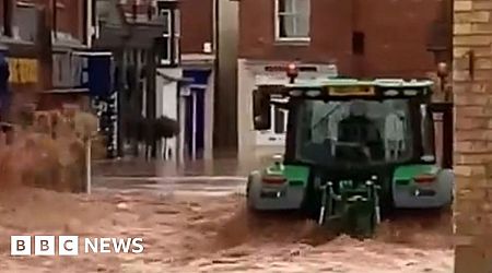 Tractor drives through flooded town, causing waves to hit shop windows