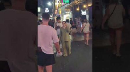 A tall gentleman with an impressive tattoo tied the shoes of a woman on a walking street in Pattaya